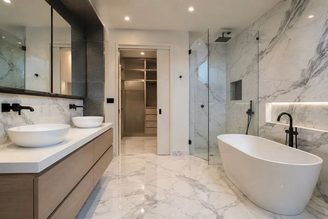 Modern luxury bathroom with marble walls, double vanity, glass shower, and freestanding tub.
