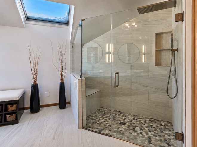 Modern bathroom with glass walk-in shower, stone tile, and decorative vases by a small window