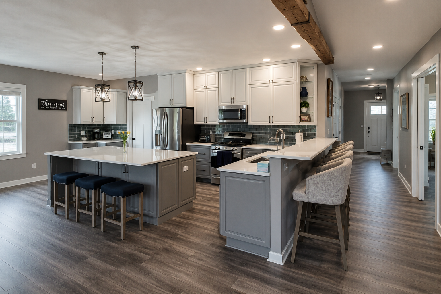 Modern kitchen with white cabinets, gray island, bar stools, stainless appliances, and dark wood floors