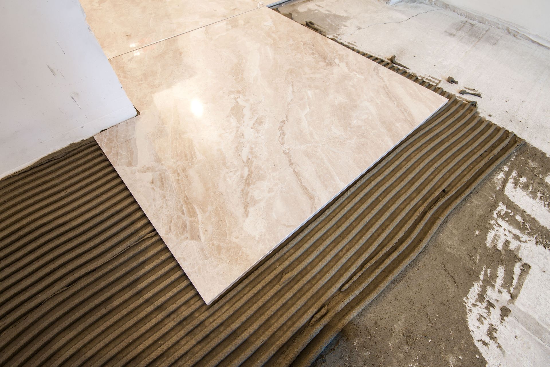 Tile being installed over ridged adhesive mortar on a floor corner.