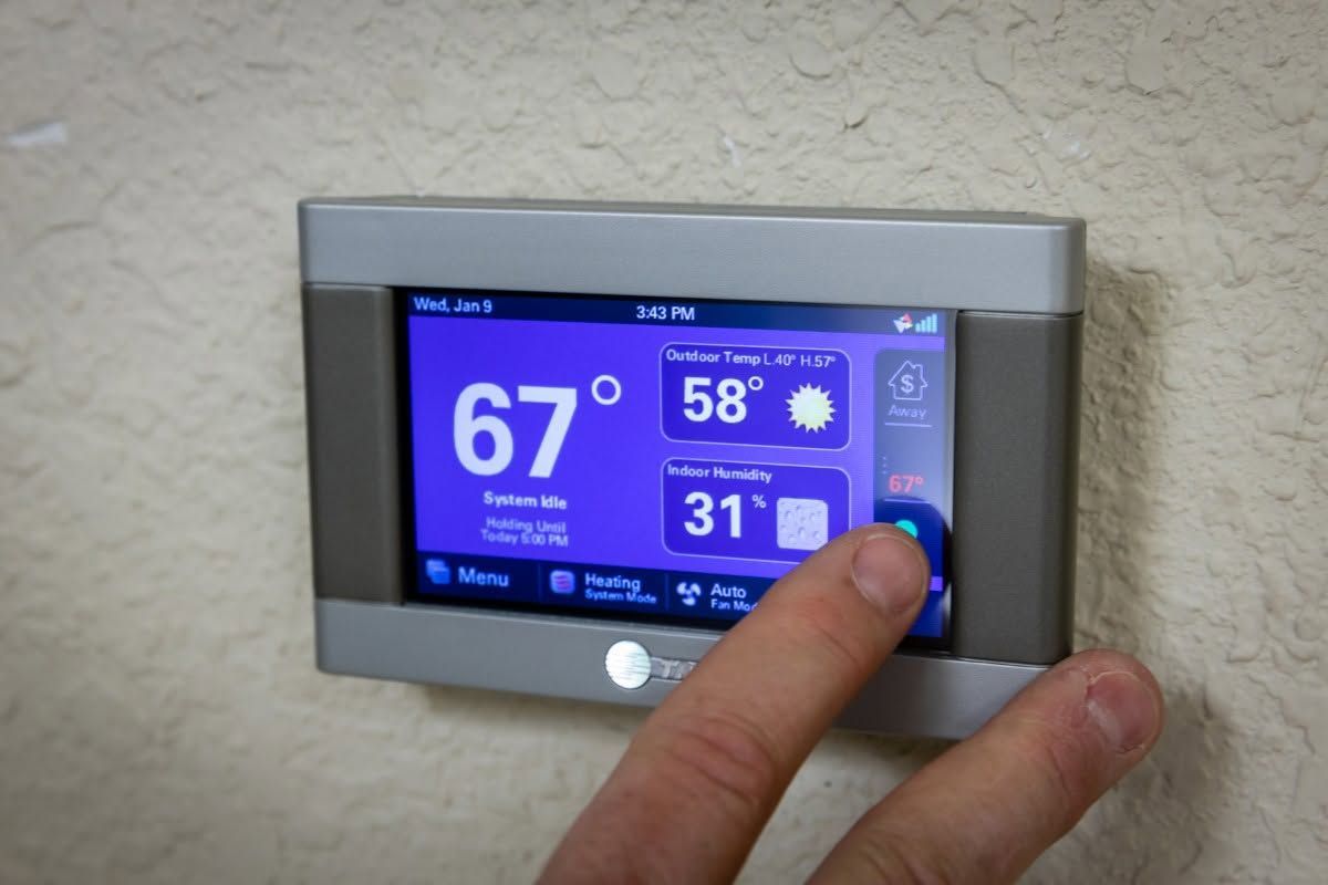 Hand adjusting a blue digital thermostat mounted on a beige wall.
