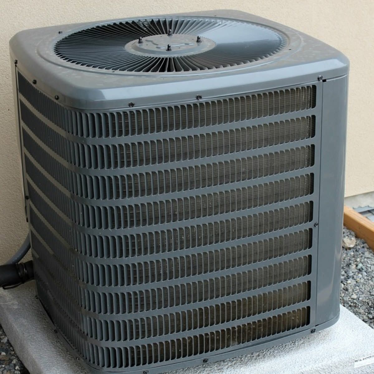 Gray outdoor air conditioner unit on a concrete pad beside a wall