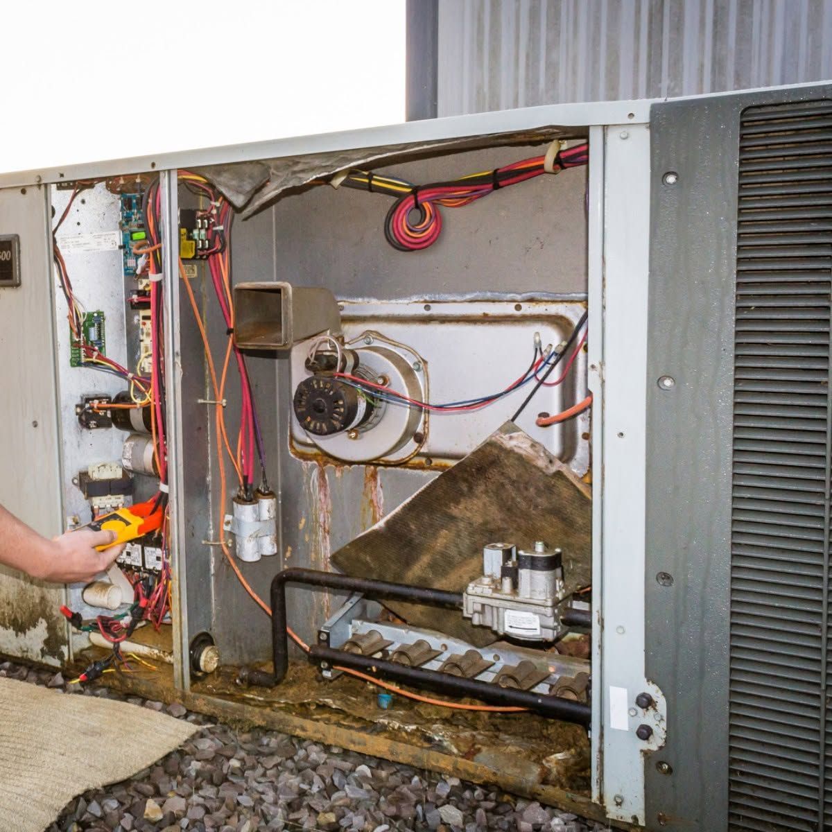 Open furnace compartment with exposed wiring, blower, and tools during maintenance
