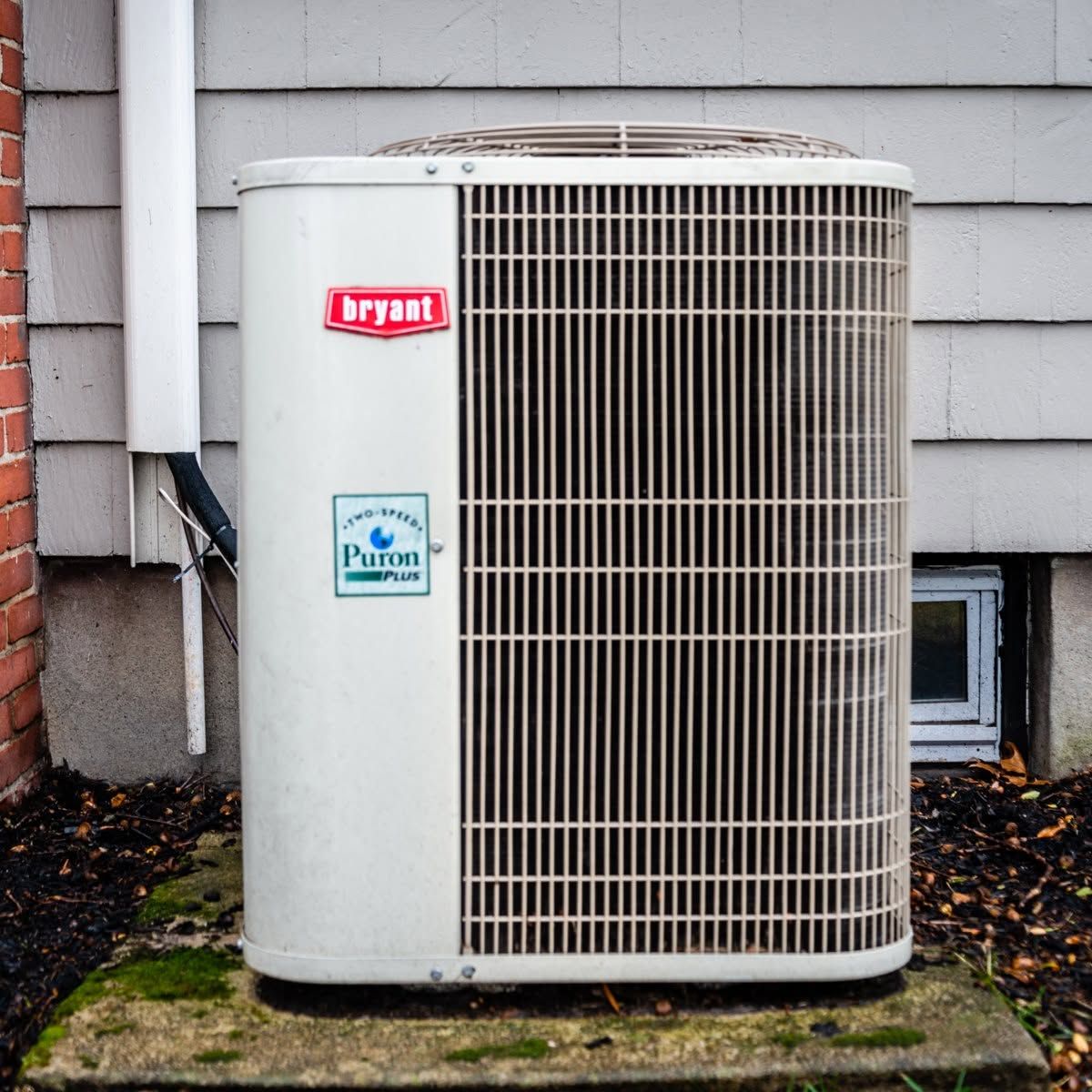 Outdoor Bryant air conditioner unit beside a house wall and basement window.