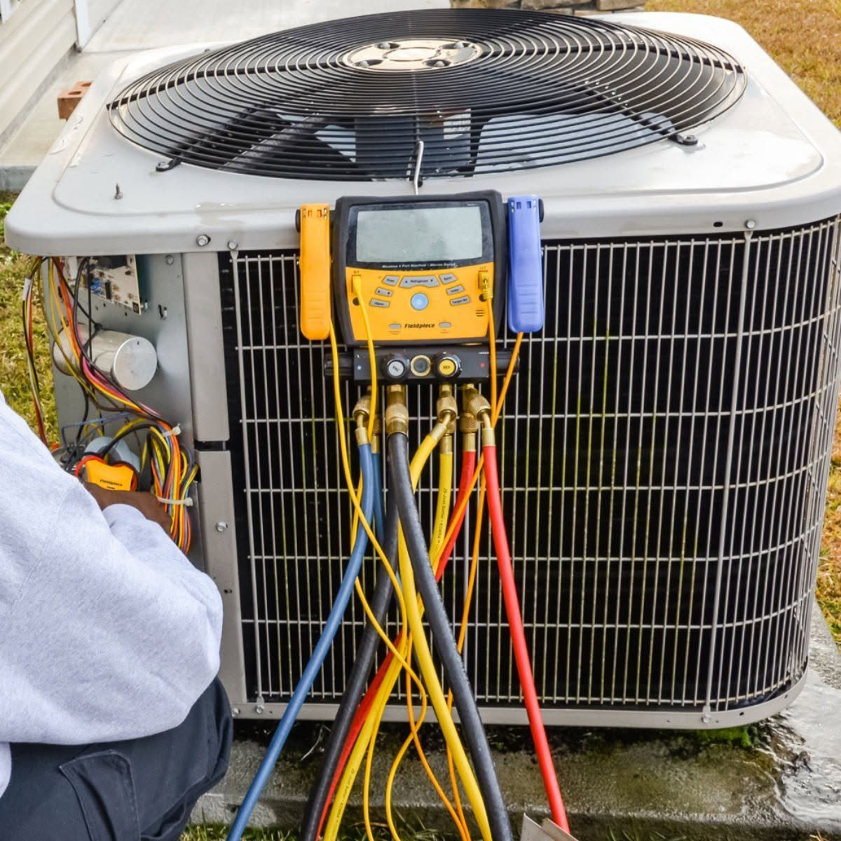 HVAC technician testing an outdoor air conditioner with gauges and hoses attached
