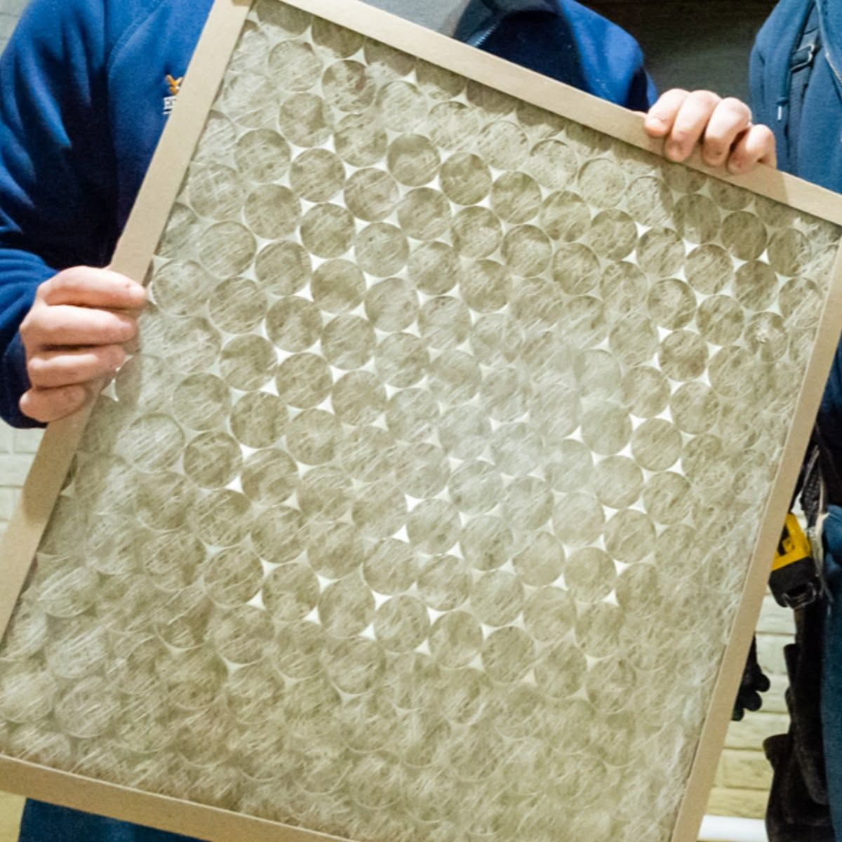 Person holding a framed panel of clear plastic bottle bottoms arranged in a grid