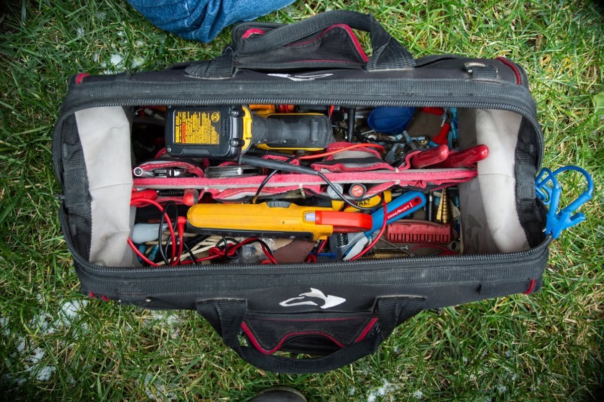 Open equipment bag on grass with red cables, tools, and battery pack inside
