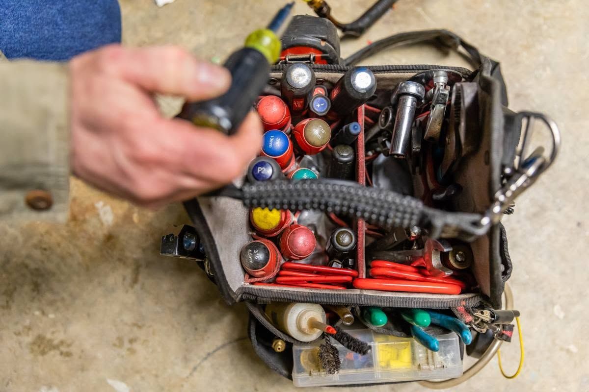 Hand using a screwdriver on a tray of assorted small tools and colorful parts
