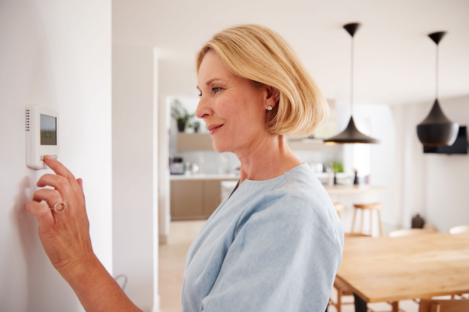 Woman adjusting a wall thermostat in a bright modern home interior