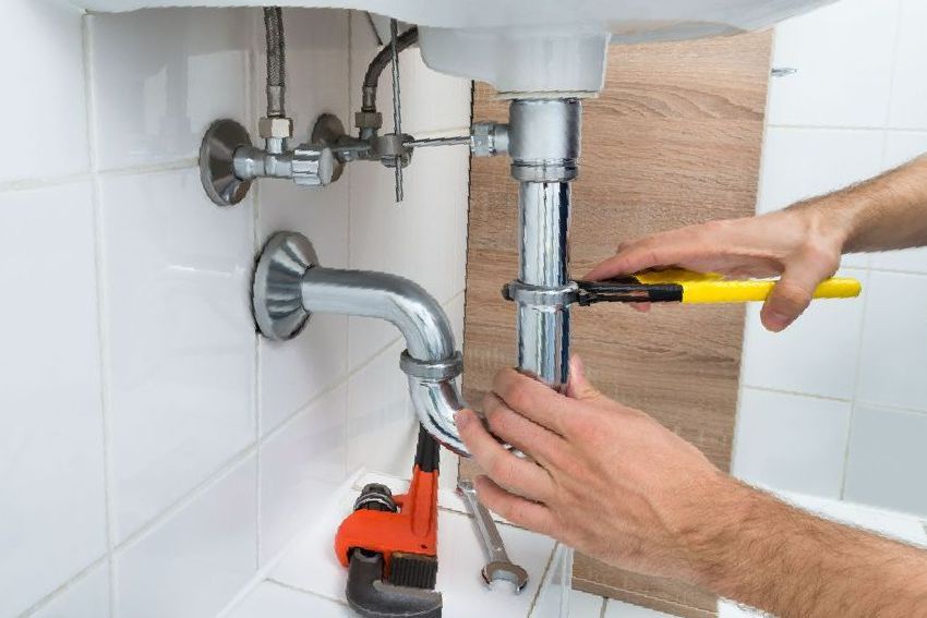 A plumber is fixing a sink pipe in a bathroom.