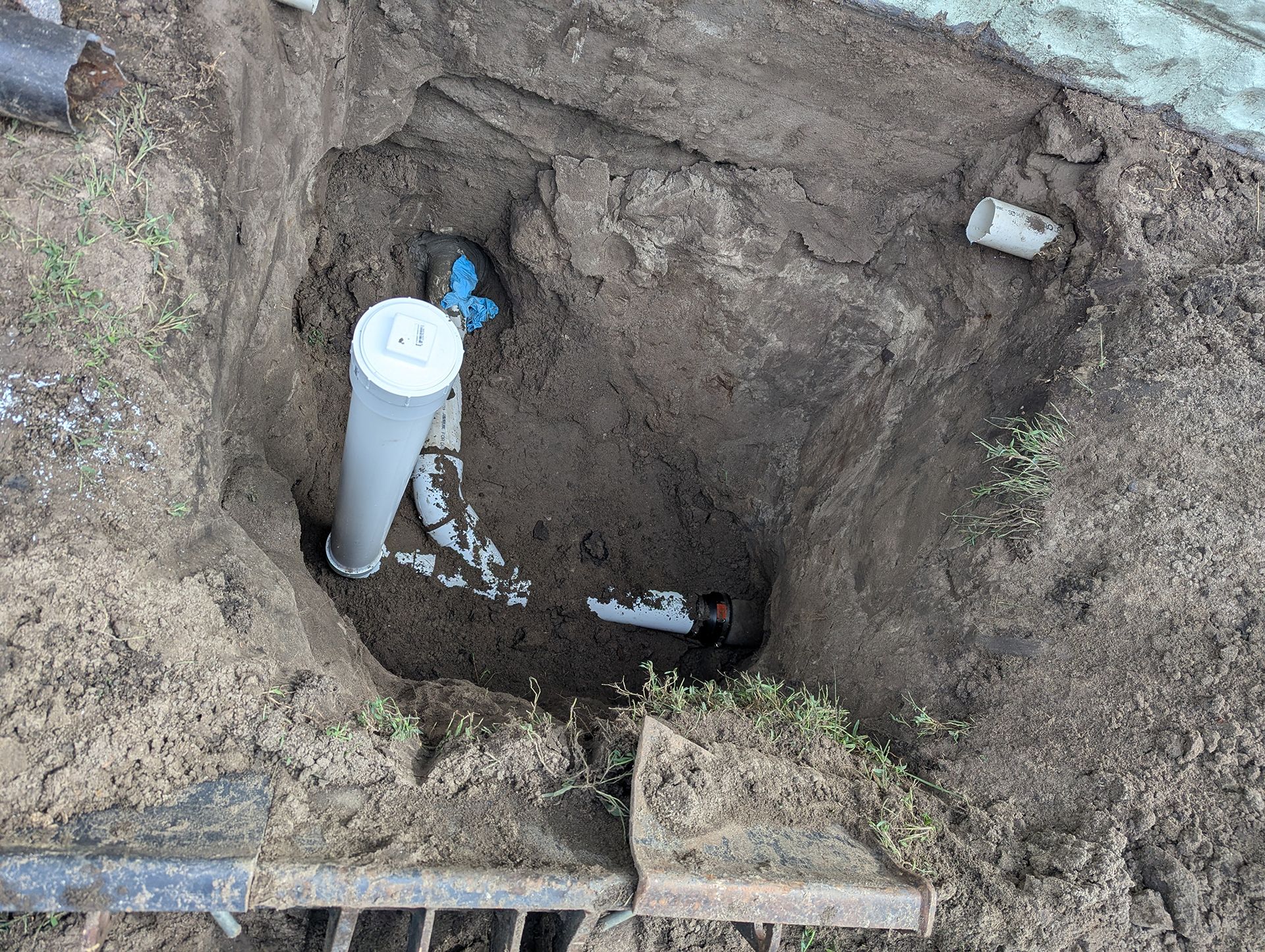 a hole in the ground reveals plumbing pipes with a white capped vent pipe