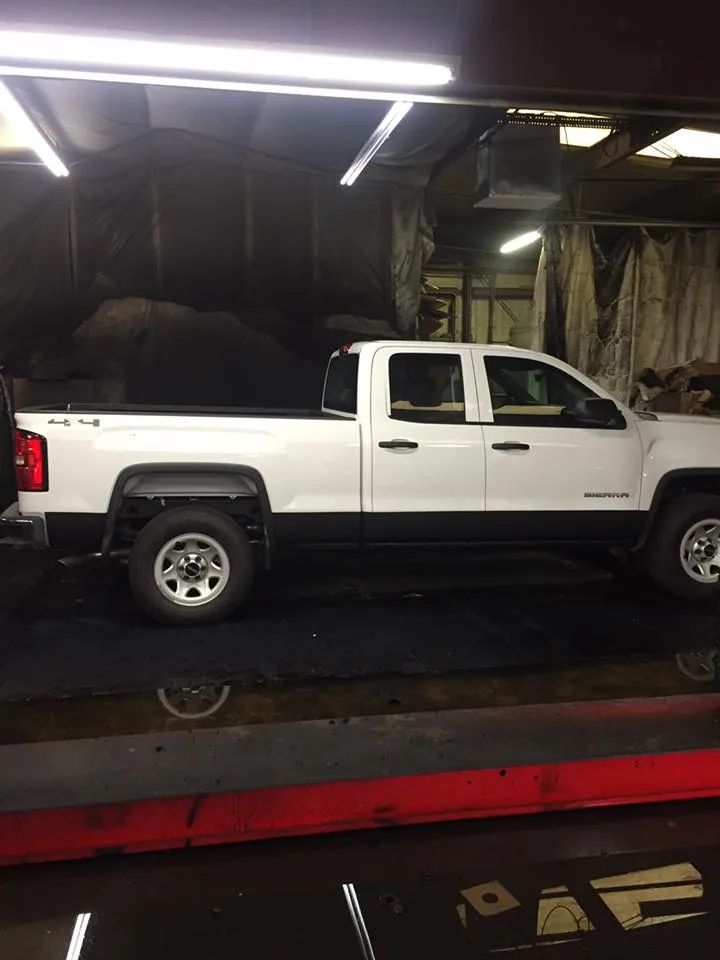 White pickup truck in a garage; black trim, silver wheels, and the bed is open to show the wheel.