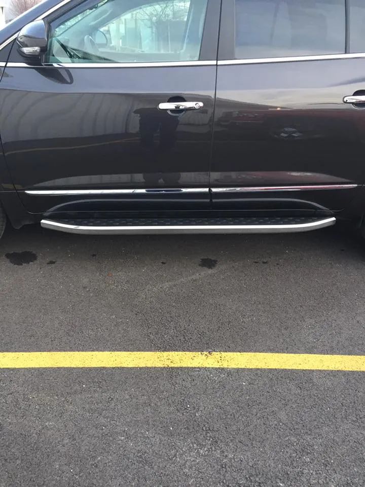 Dark SUV with a running board parked on asphalt next to a yellow line.