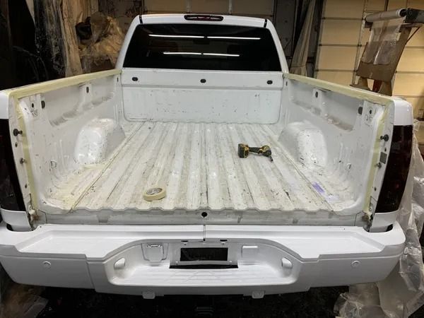 White truck bed, empty, with a white bumper. The truck is inside a garage.