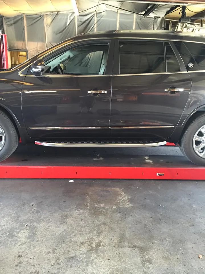 Dark SUV on a red lift. Chrome running boards, and wheels are visible, in a garage setting.