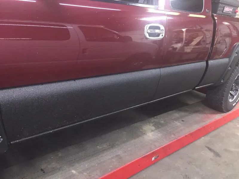Maroon pickup truck with black textured lower panels, on a lift in a shop.