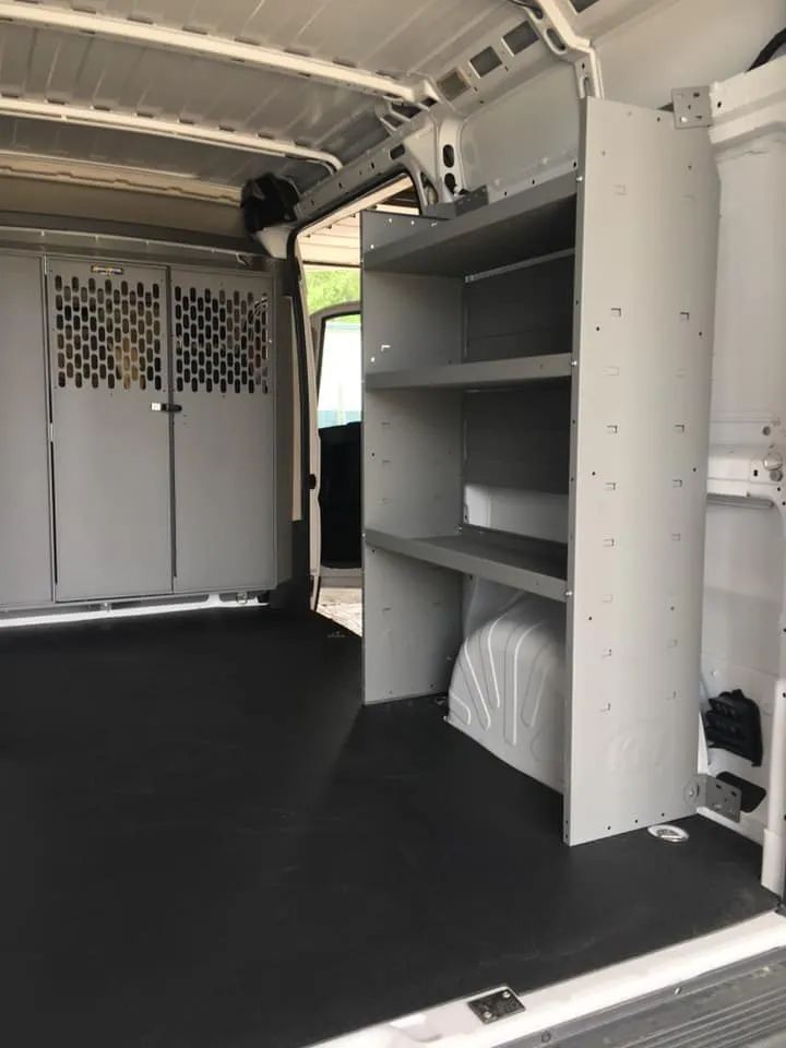 Interior of a white work van with gray shelving and a caged partition. Black flooring.