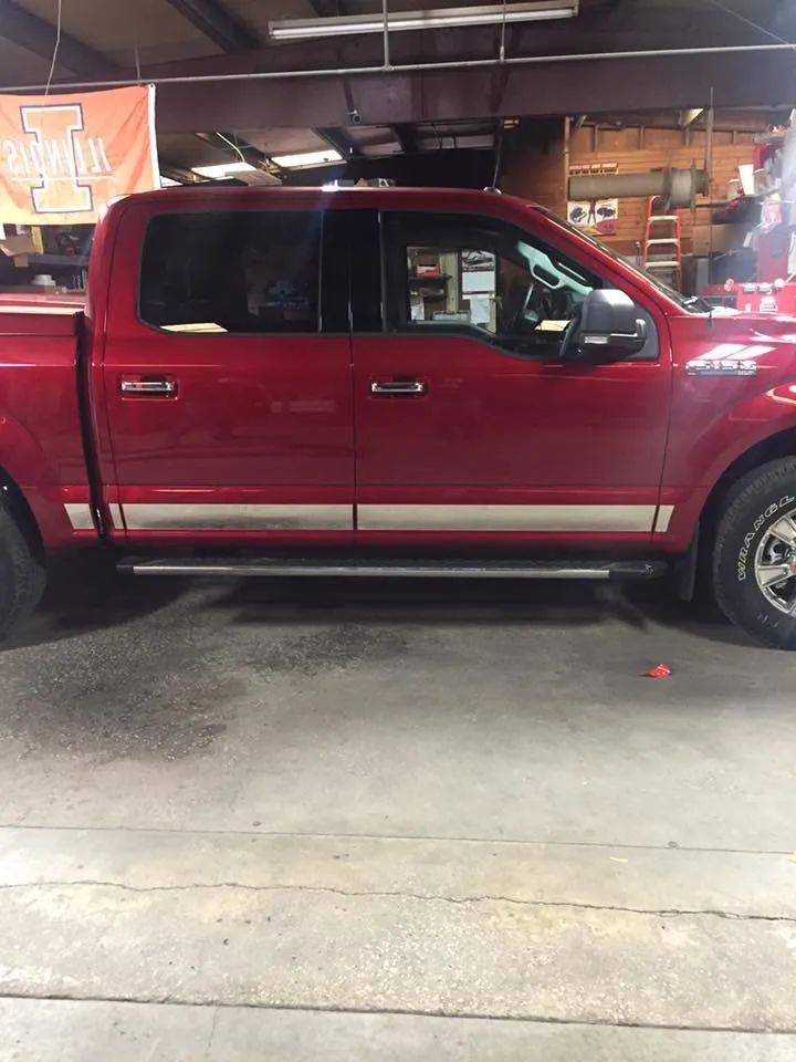 Red Ford F-150 pickup truck with silver side accents parked indoors, next to a concrete floor and a University of Illinois banner.