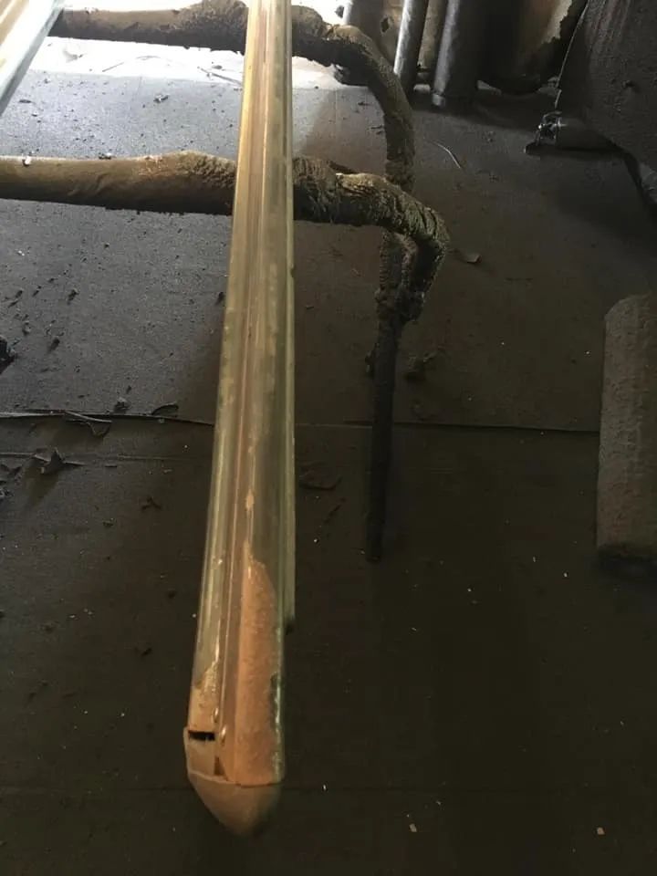 Metal industrial pipe, partially rusted, on a dark floor with additional metal structures in the background.