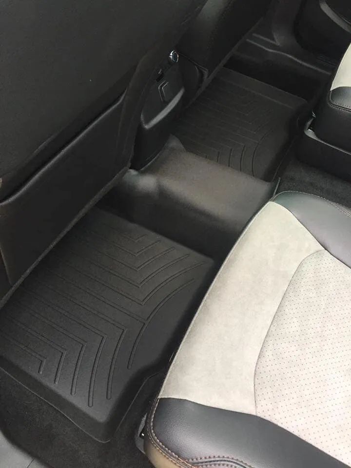 Black rubber floor mats in a car's back seat. Light-colored seats are visible.