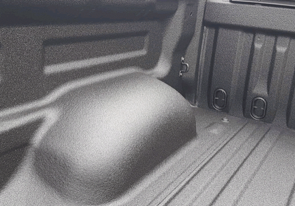 Textured black truck bed with wheel well and tie-down rings.