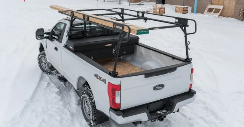White Ford pickup truck with ladder rack on snowy ground.