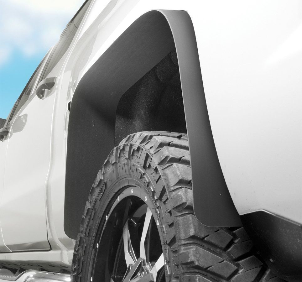 White truck's rear wheel and black fender flare over a large off-road tire.