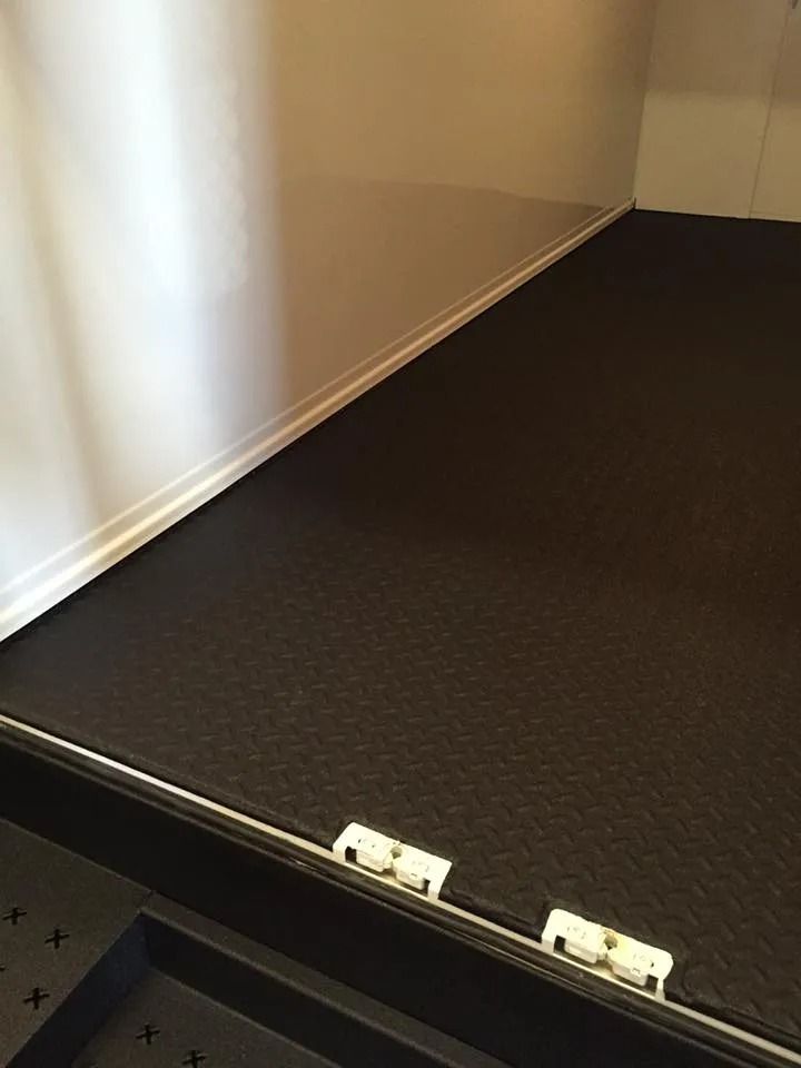 Black textured flooring against a white wall with white trim. Two white hinges visible.