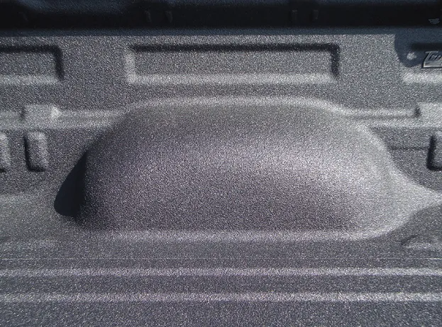 Close-up of a truck bed with a textured, gray bed liner and wheel well.
