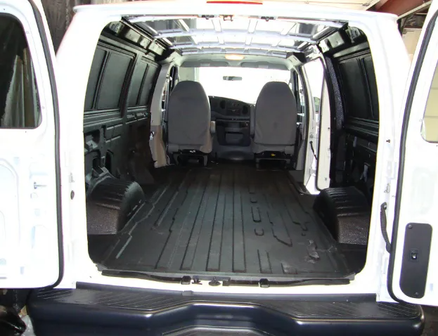 Interior of a white cargo van with black floor mat, open doors, and two front seats.