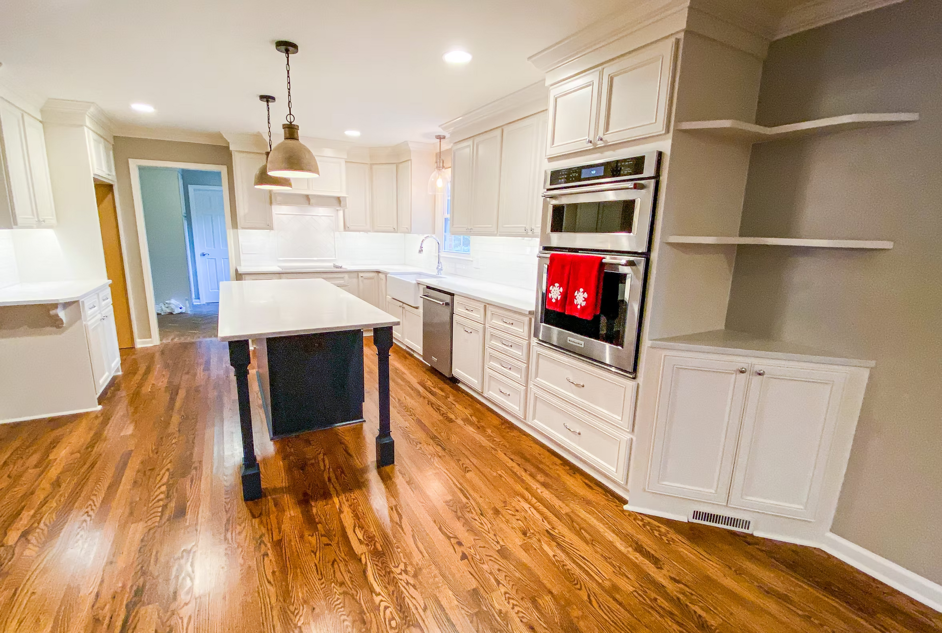 A renovated kitchen with light cabinetry, stainless steel appliances, and a dark island. Warm wood flooring and recessed lighting create a bright space.