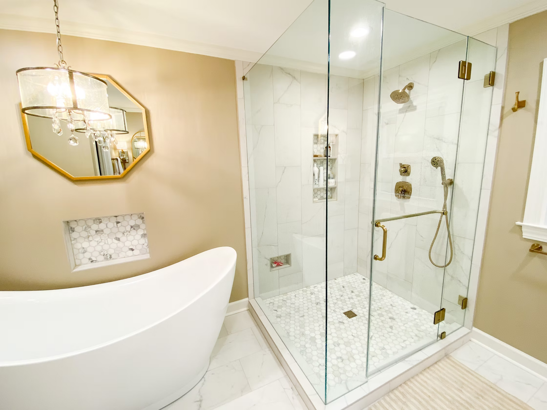 Modern bathroom with a glass-walled shower, freestanding tub, and gold fixtures. Beige walls and white tile flooring complete the spa-like design.