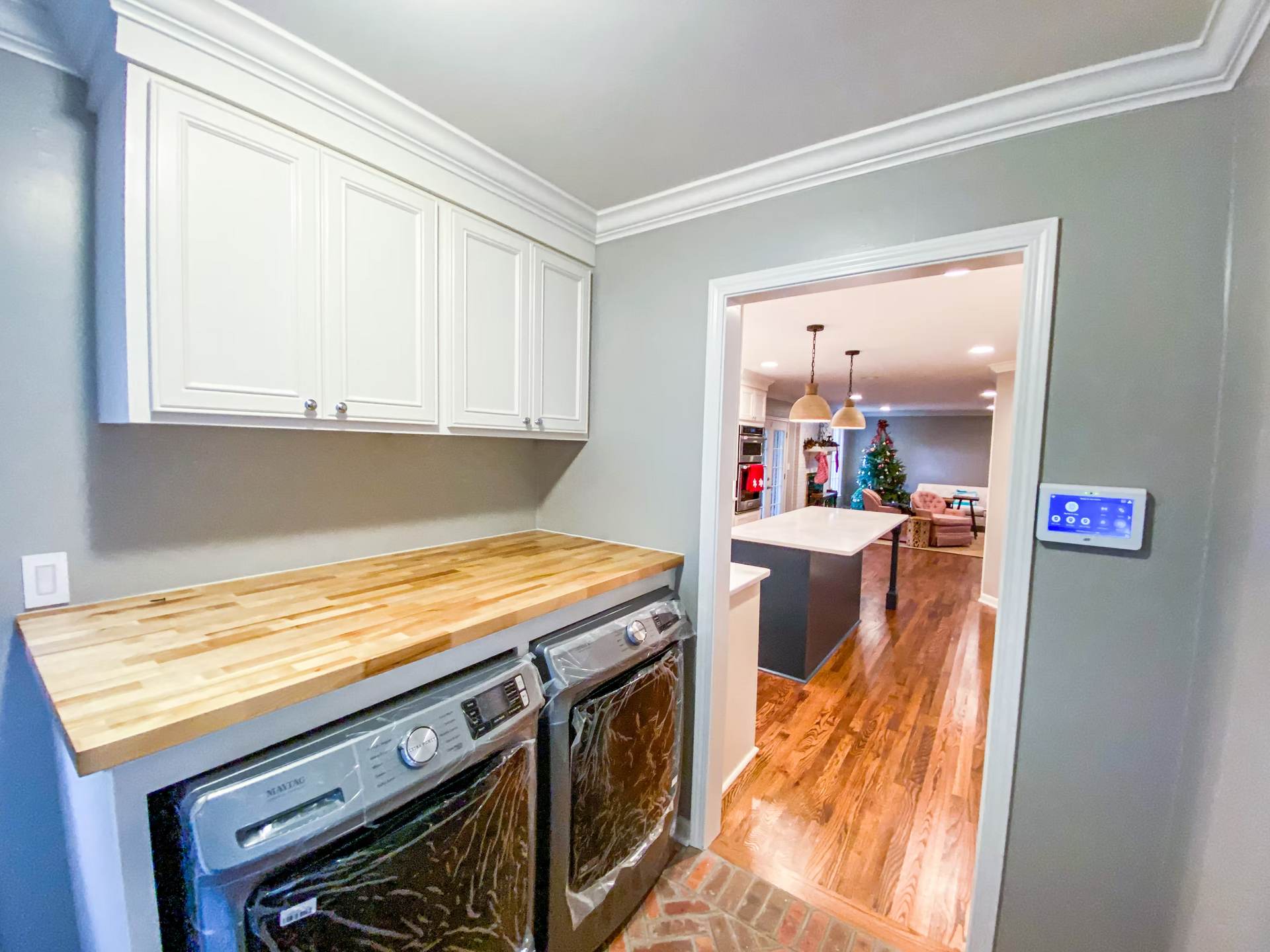 Laundry room with white cabinets, a wood countertop over a washer and dryer, and a doorway to a kitchen.