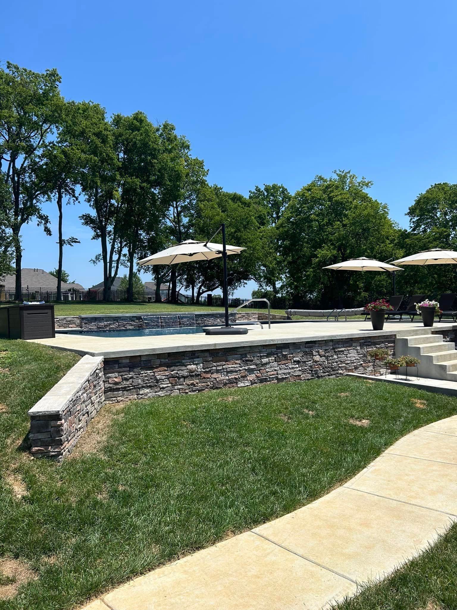 A walkway leading to a large swimming pool surrounded by trees and umbrellas.