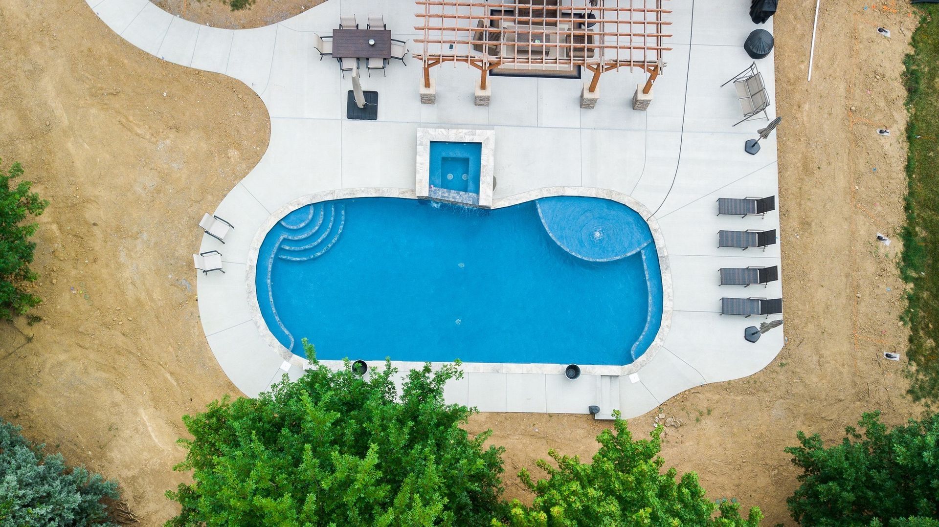 An aerial view of a large swimming pool in a backyard surrounded by trees.