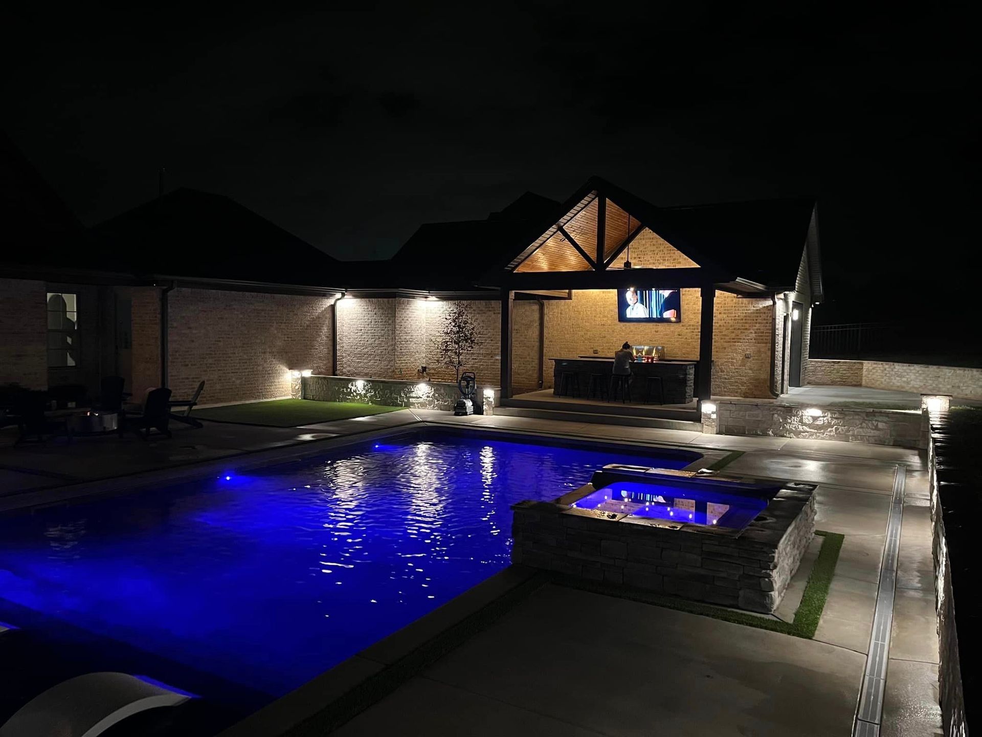 A large swimming pool is lit up at night in front of a house.