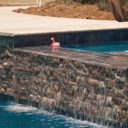 A pink flamingo is floating in a pool next to a waterfall