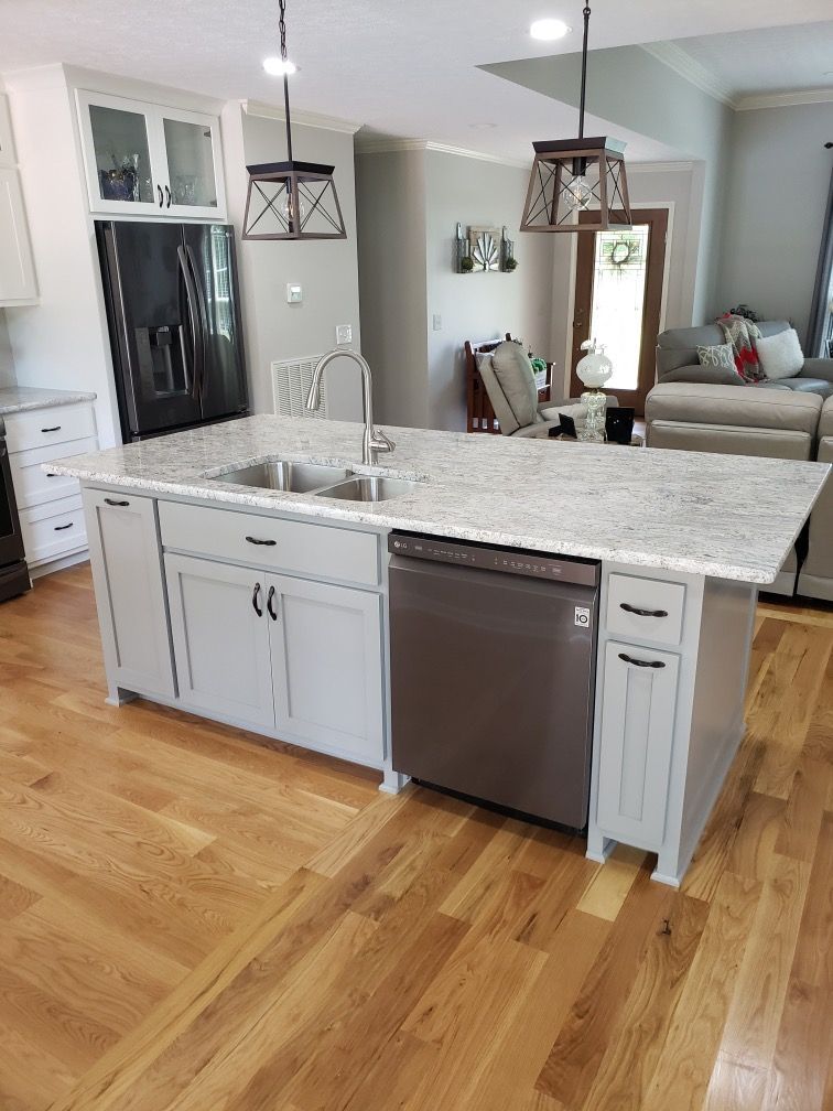 A kitchen with a large island, sink, dishwasher, and cabinets.