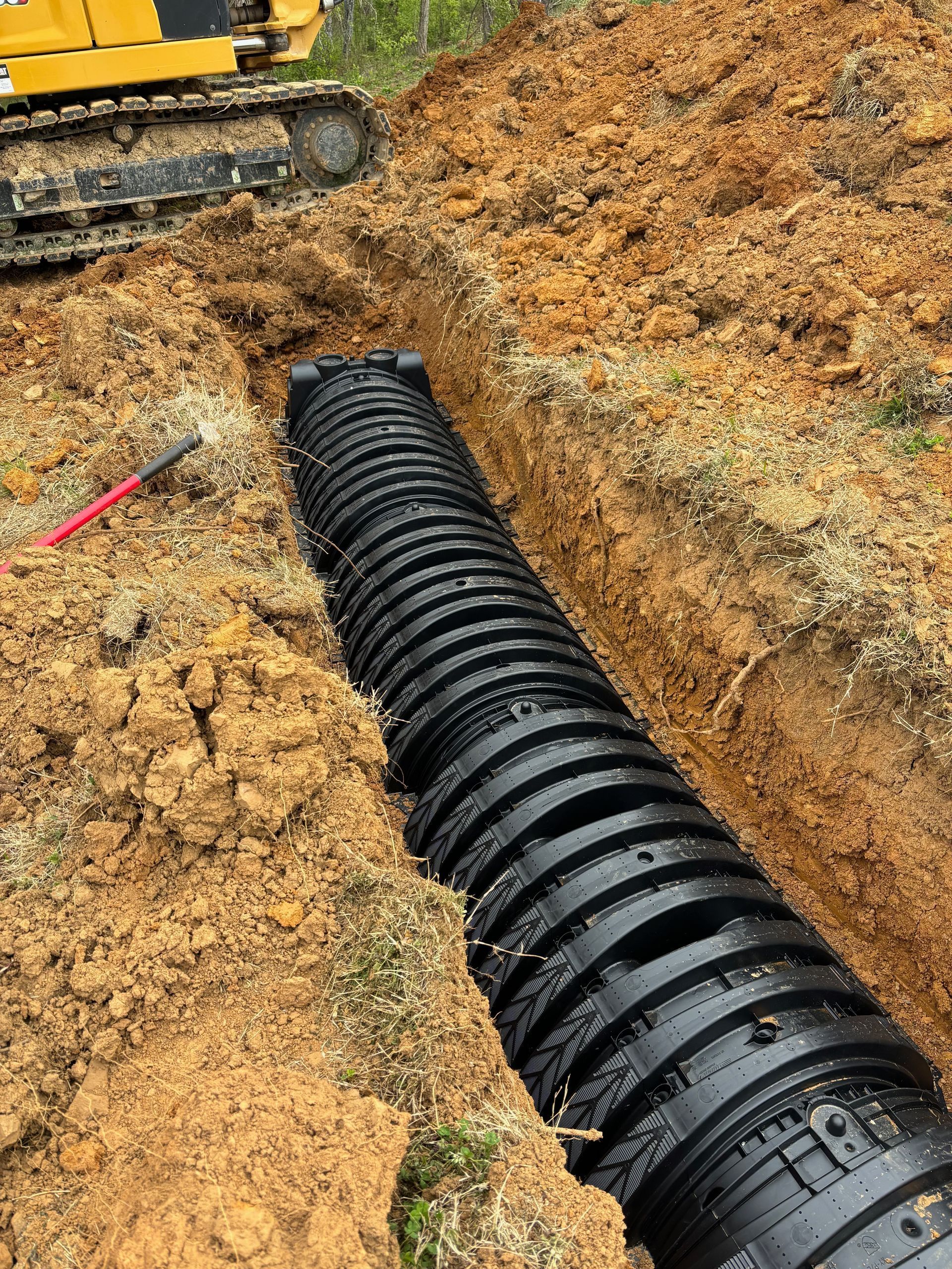 A large black pipe is being installed in the dirt.
