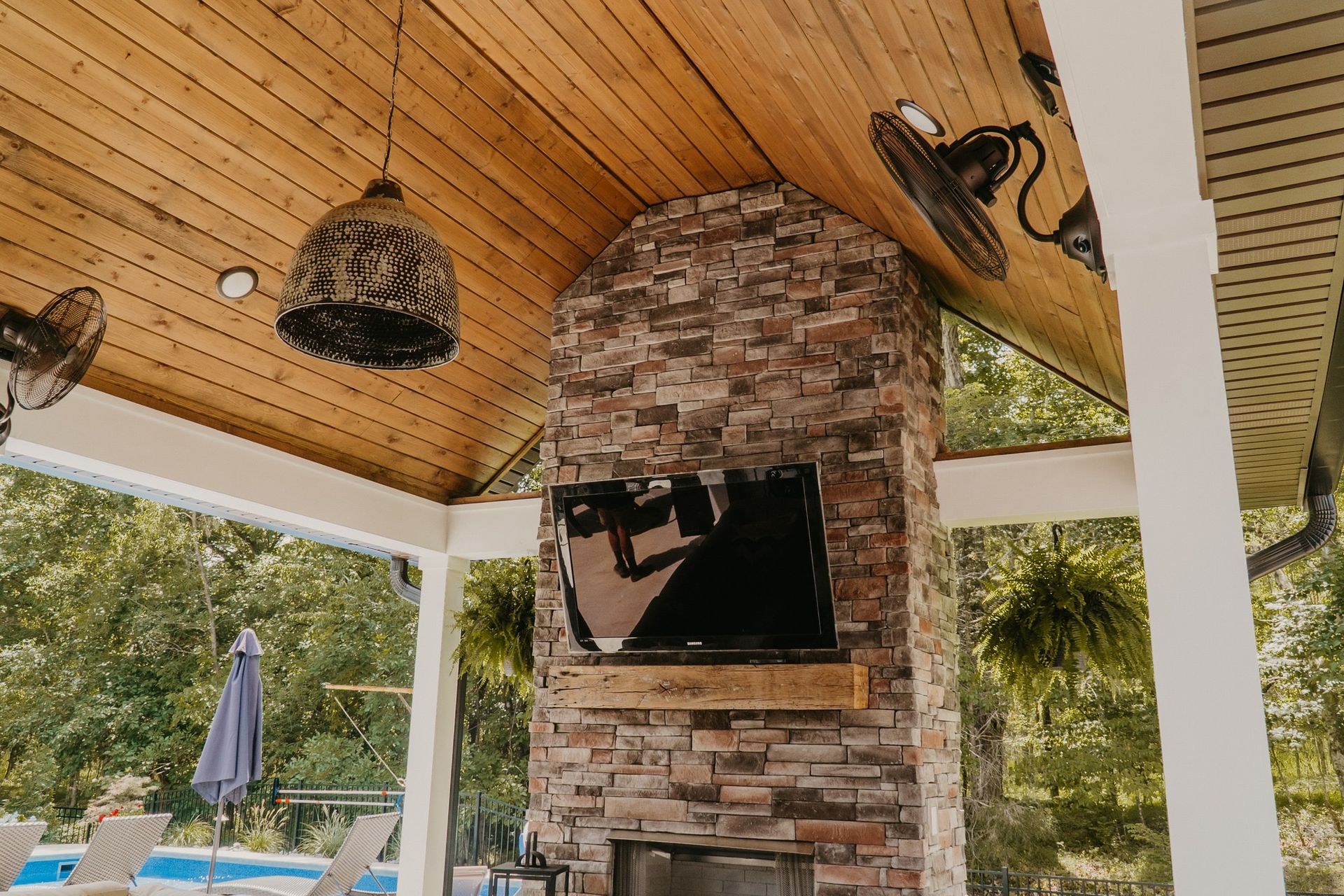 A covered patio with a fireplace and a flat screen tv.