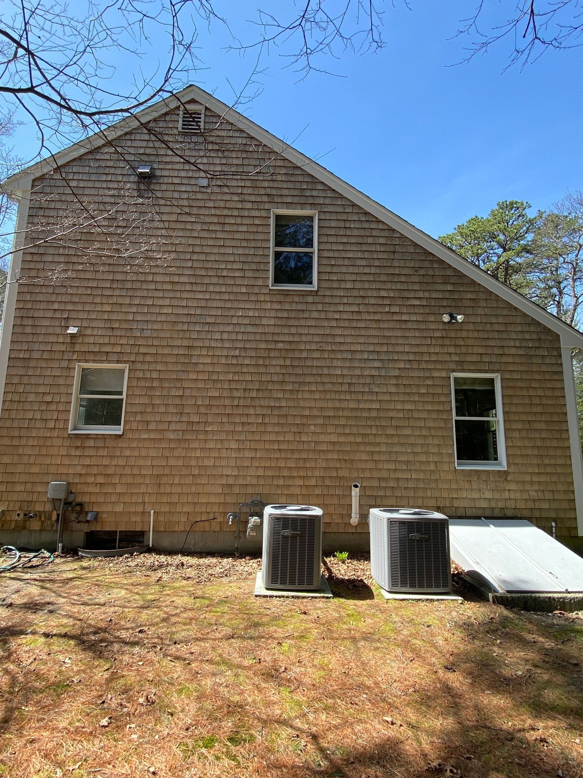 Side view of a two-story house with weathered wood siding, windows, and two air conditioning units.