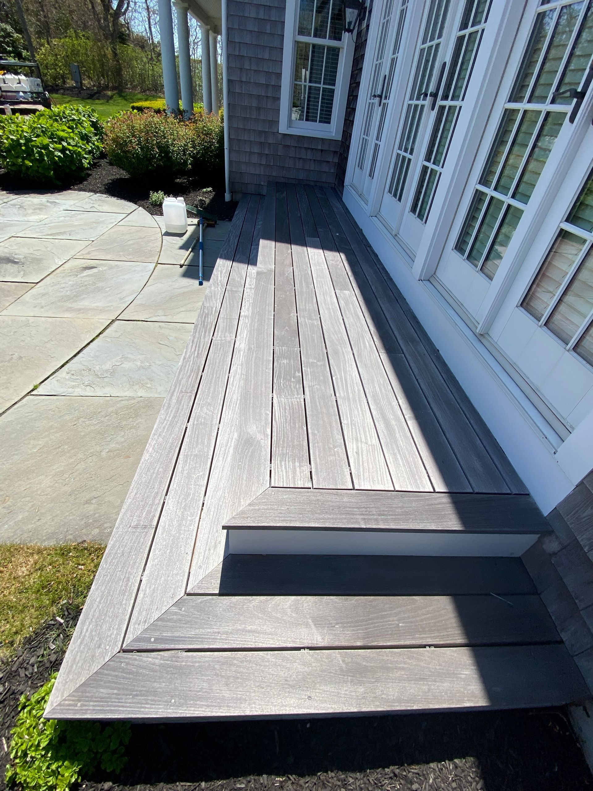 Wooden deck with steps beside a house with white trim and windows.