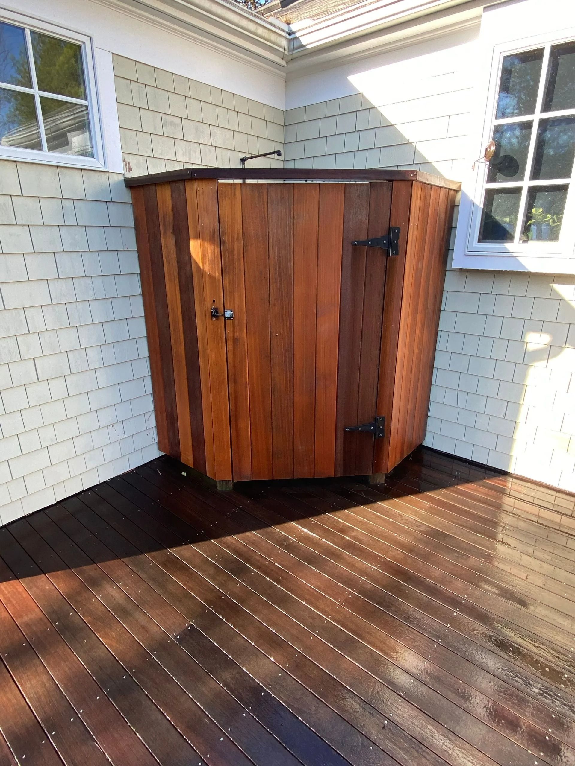 Wooden outdoor shower on a deck, set against a light green house.