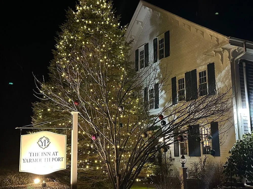 Night view of The Inn at Yarmouth Port with holiday lights and a sign.