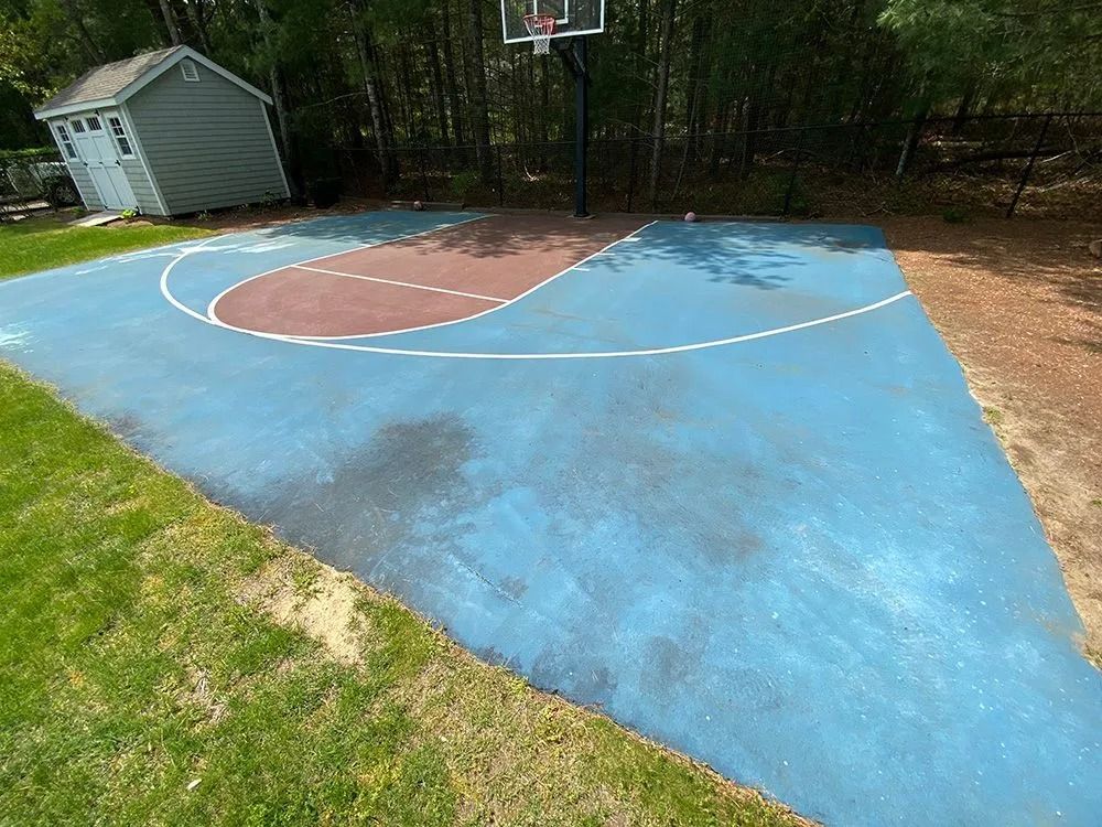 Blue basketball court with brown and white details, a hoop, and a small shed in a yard.