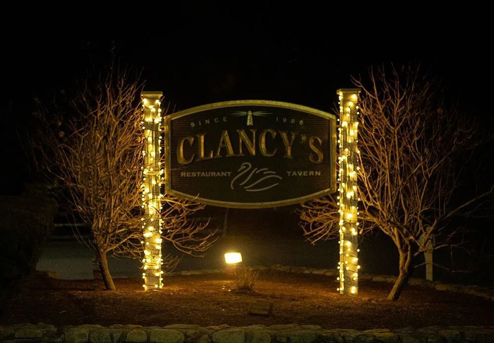 Clancy's Restaurant & Tavern sign lit up at night, with trees decorated with fairy lights on either side.