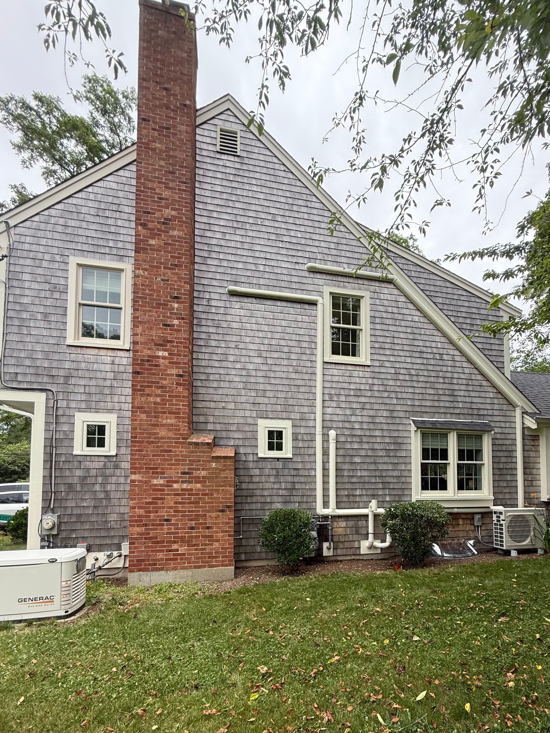 Side of a house with cedar shake siding, a brick chimney, and a generator on the lawn.