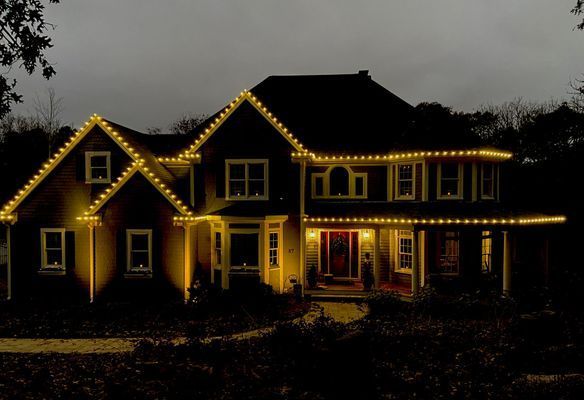 House at night with yellow Christmas lights outlining roof and windows.