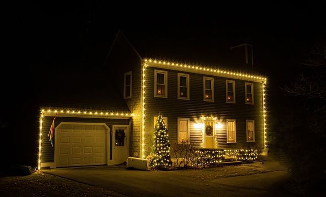 House at night with Christmas lights along roofline and around windows.