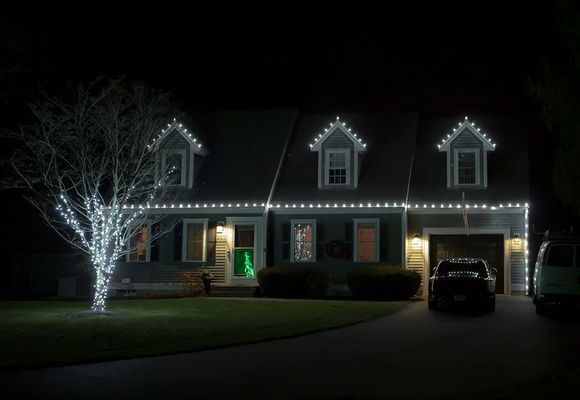 House decorated with white Christmas lights at night. A tree is lit up in the front yard.